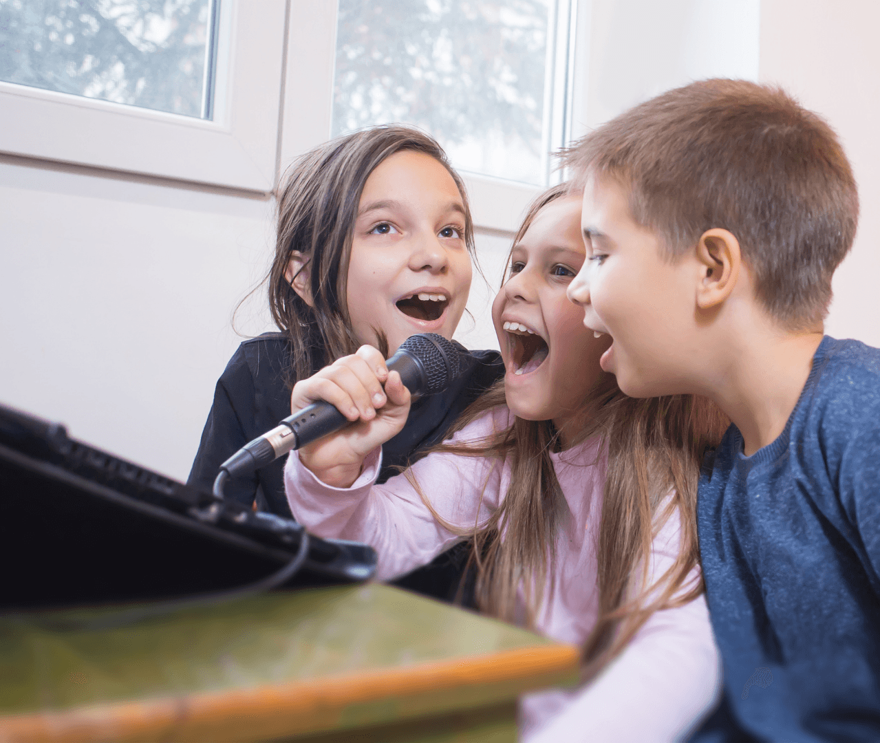 Three kids sharing a microphone and singing together.